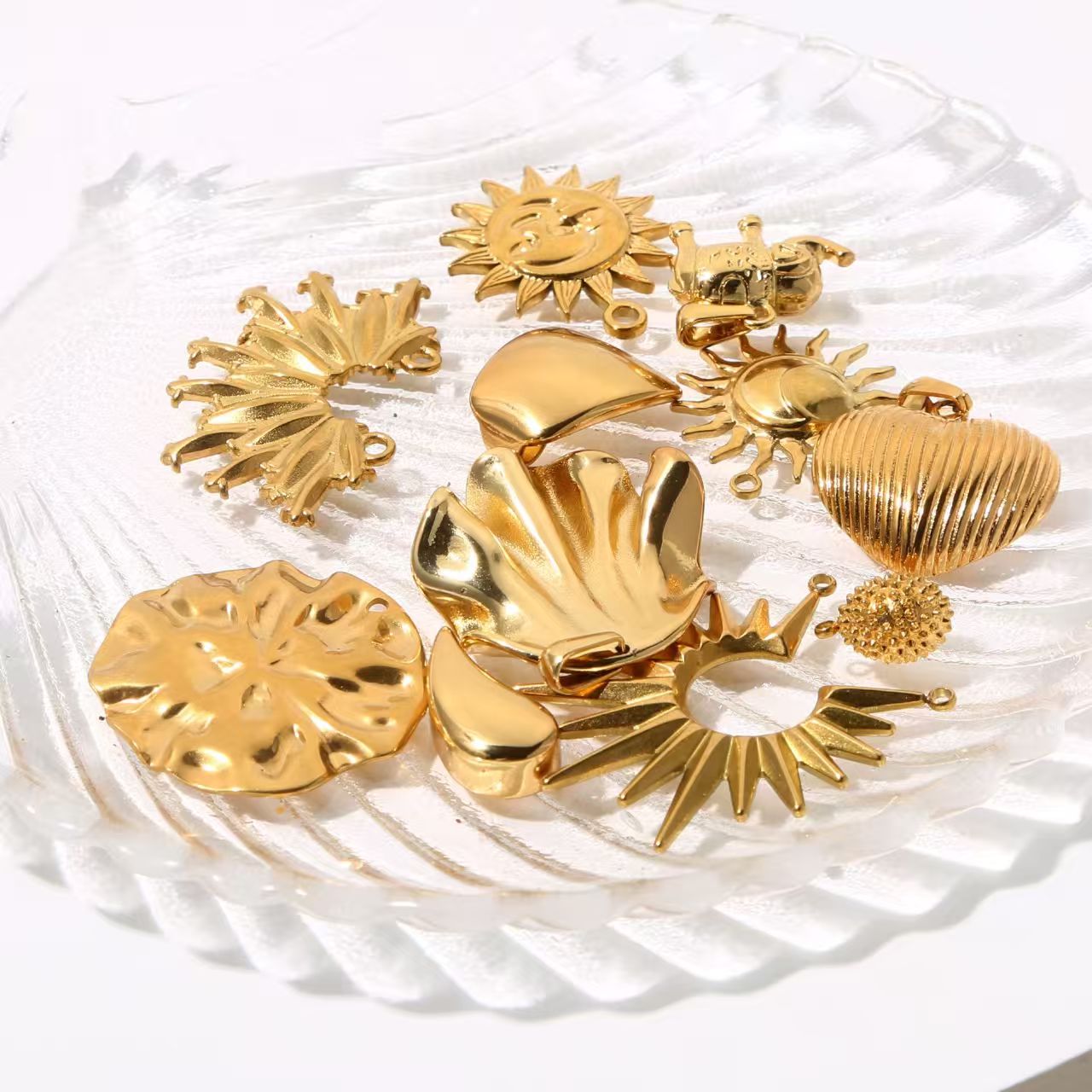 Collection of personalized gold - colored stainless - steel pendants. DIY jewelry accessories for bracelets and necklaces with multiple shapes like sun, heart, and elephant. 5 pieces in total.