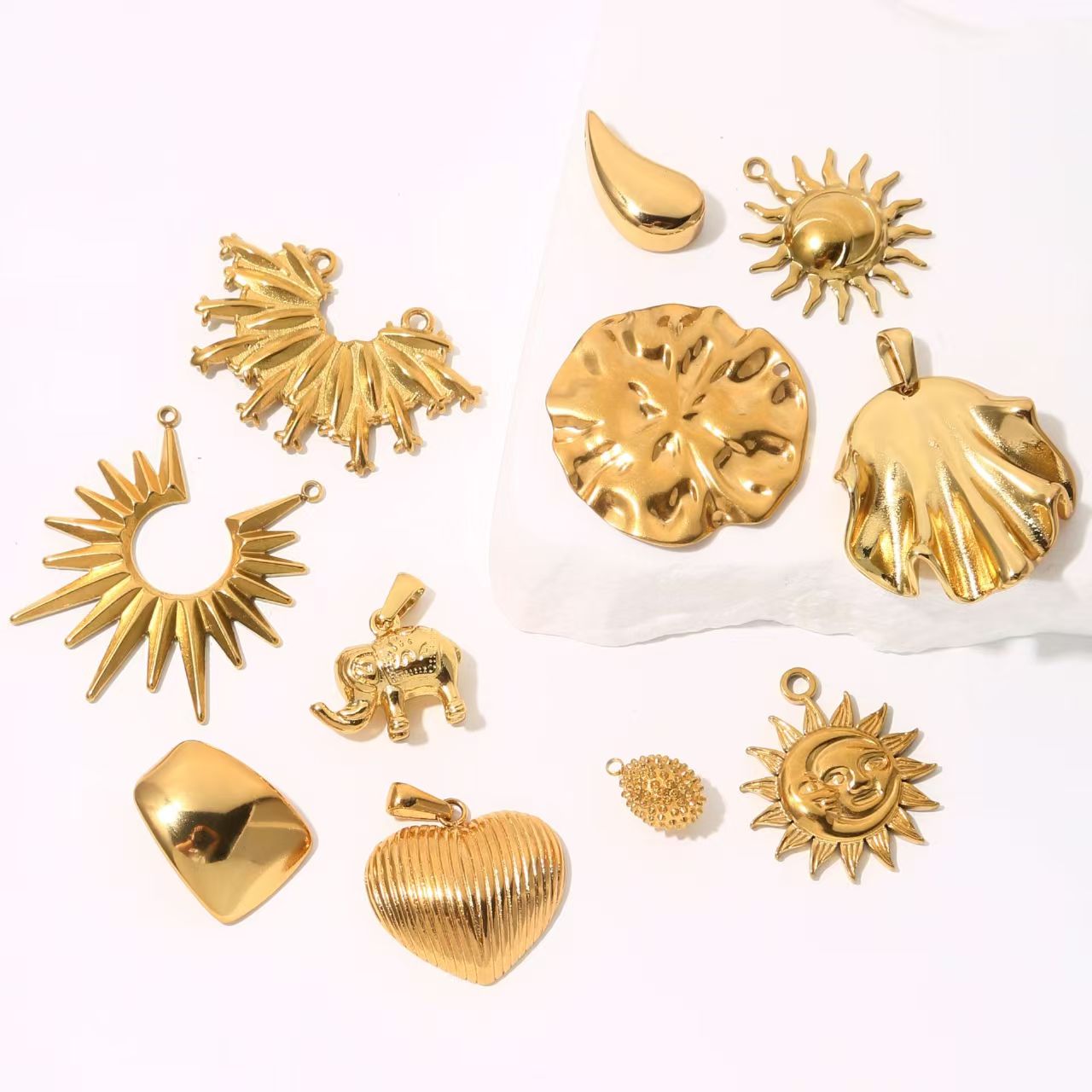 Collection of personalized gold - colored stainless - steel pendants. DIY jewelry accessories for bracelets and necklaces with multiple shapes like sun, heart, and elephant. 5 pieces in total.